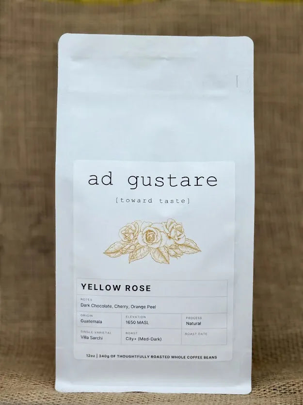 Ad Gustare Yellow Rose Guatemala coffee bag with minimalist white label featuring a yellow rose illustration, photographed on burlap. Front view