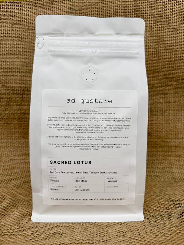 White coffee bag labeled ‘Ad Gustare World Coffee Tour – Vietnam Sacred Lotus Roast,’ featuring illustrated Vietnamese phin coffee and iced coffee on a burlap background.