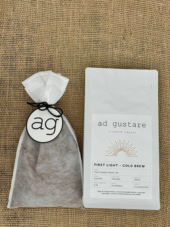 Coffee filter with 'ag' logo and a package of 'ad gustare' First Light  coffee on a textured surface
