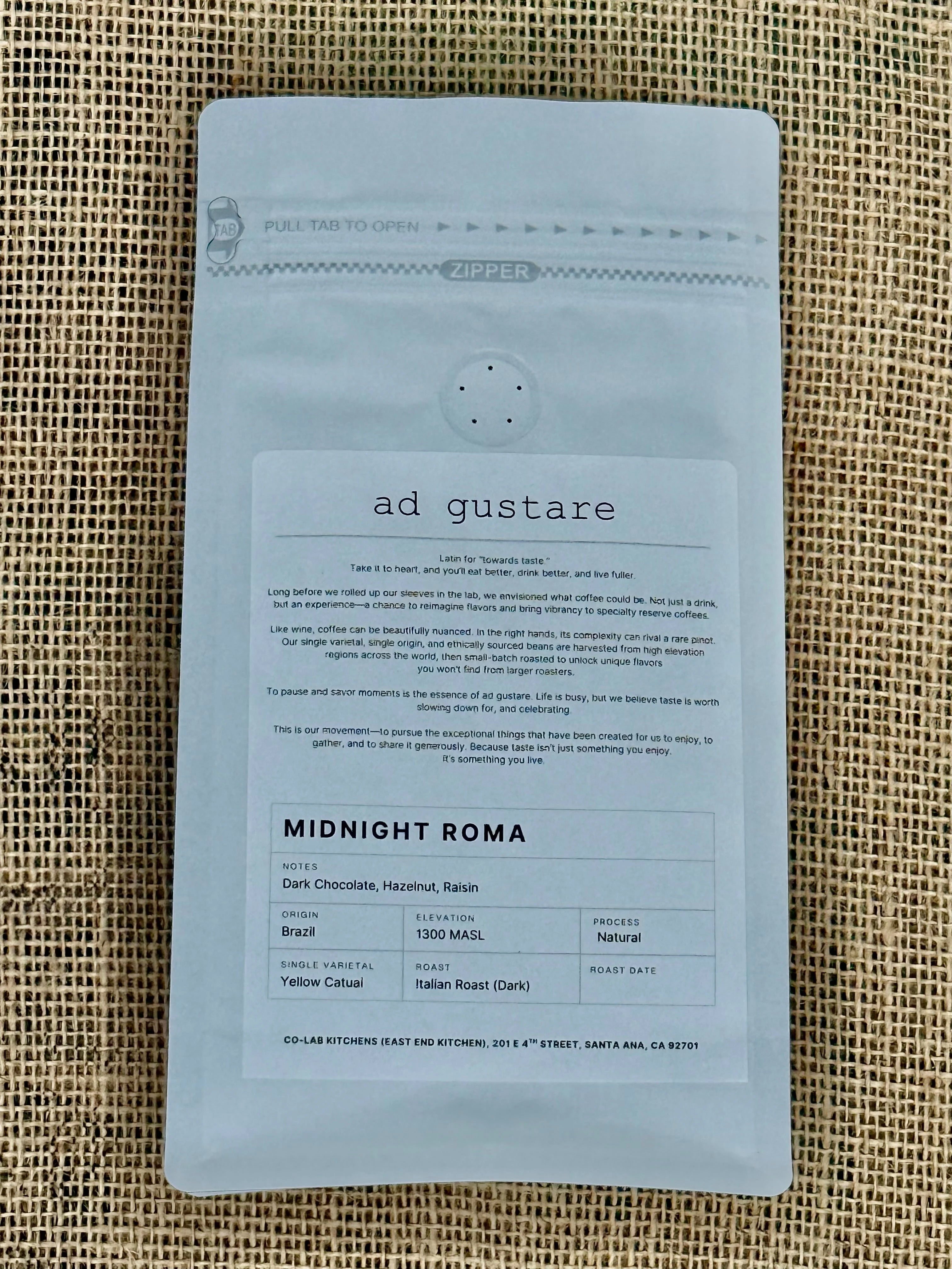 Ad Gustare World Coffee Tour Italy Midnight Roma Roast coffee bag with green, white, and red label featuring a moka pot, espresso cup, and Colosseum illustration, photographed on burlap