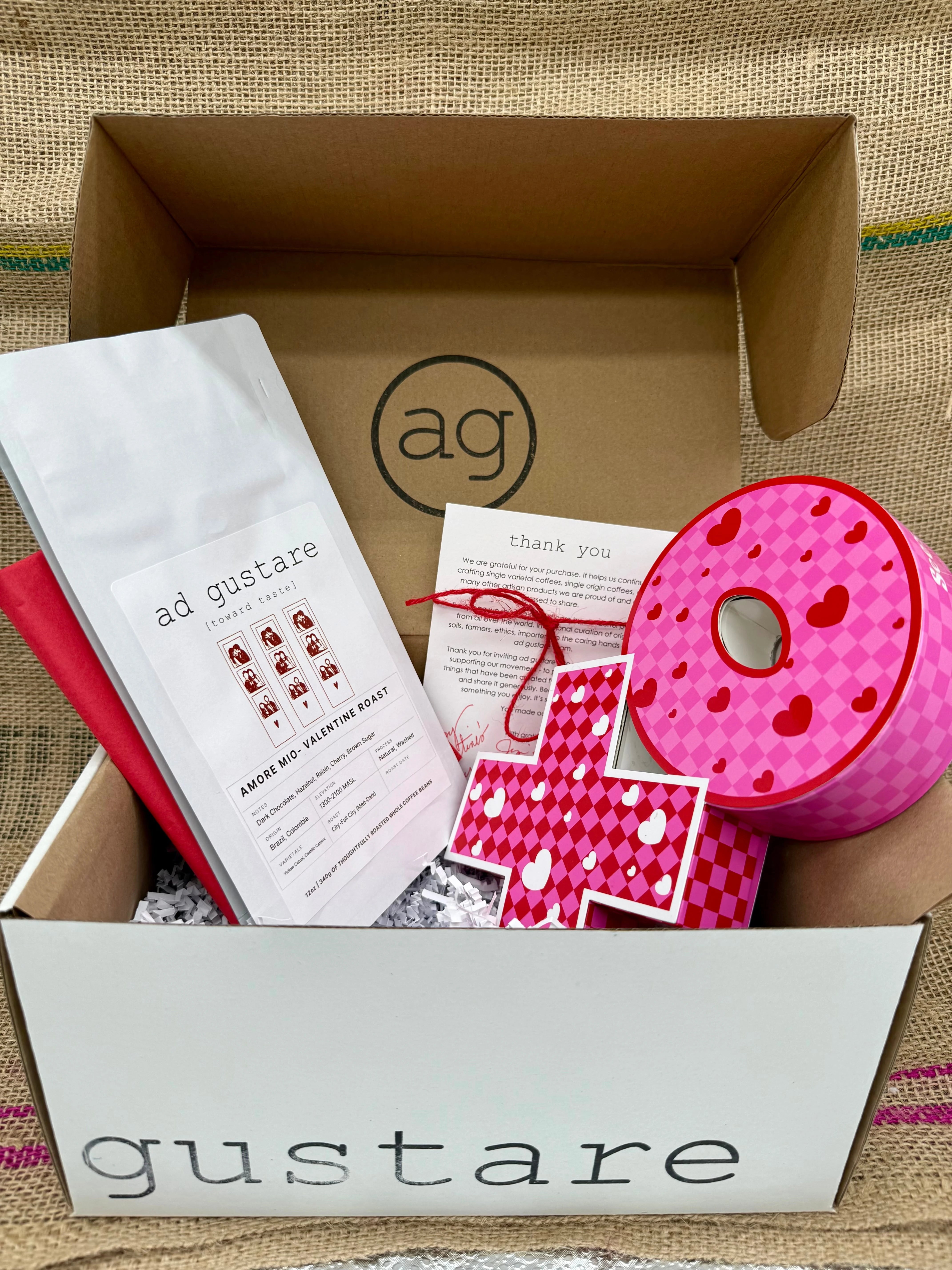 Gustare subscription box with pink donut-shaped container and branded materials on a textured surface.